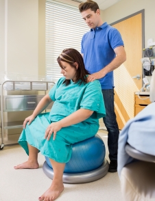 woman in labour sitting on exercise ball, with her husband massaging her neck