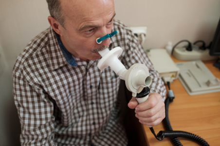Man with a nose clip, blowing into a tube for a spirometry test