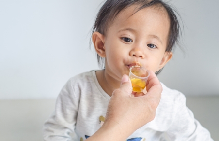 toddler taking medicine from a measuring cup
